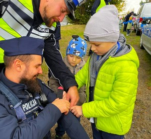 policjanci i chłopiec, który na mundur policjanta przykleja pamiątkową nalepkę