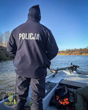 Zdjęcie przedstawia policjanta, który stoi na łódce.