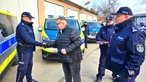 Zdjęcie przedstawia mężczyznę, który wręcza policjantowi klucze, w tle radiowozy.