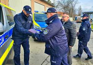 Zdjęcie przedstawia trzech mężczyzn, stojących obok radiowozu.