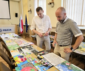 Dwóch mężczyzn stoi nad stołem, na którym leża prace dzieci.