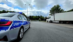 Zdjęcie przedstawia radiowóz, za nim ciężarówki.