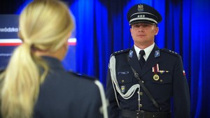 Policjant stoi na baczność n a niebieskim tle.