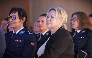 Kobiety siedzą obok siebie, jedna jest w mundurze.