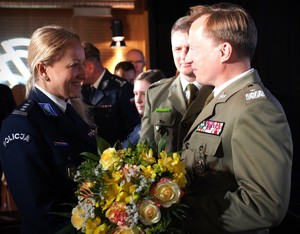 Mężczyzna wręcza kobiecie w mundurze kwiaty.