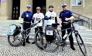 Czterech mężczyzn dwóch stoi przy rowerze, dwóch w mundurze.