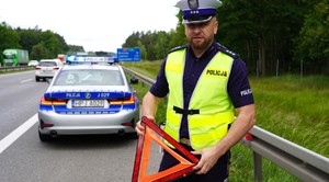 Policjant z trójkątem, przed radiowozem.