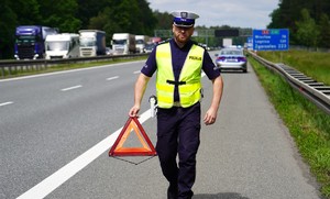 Policjant idzie autostrada z trójkątem bezpieczeństwa.