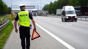 Policjant stoi tyłem na autostradzie, w ręku trzyma trójkąt bezpieczeństwa.
