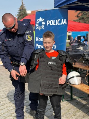 Policjant pomaga ubrać dziecku sprzęt służbowy.