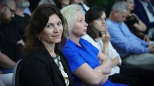 Trzy kobiety słuchające wykładu, jedna uśmiecha się.