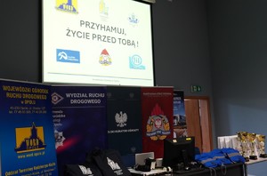 Na ekranie telebim z napisem &quot;Przyhamuj, życie przed Tobą&quot;, pod nim banery różnych instytucji, medale i puchary.