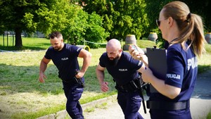 Policjanci biegną, obok policjantka mierzy czas.