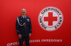 wyróżniony medalem policjant na tle baneru z logo Honorowego Krwiodowstwa