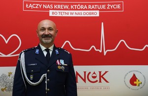 wyróżniony medalem policjant na tle baneru z logo Honorowego Krwiodowstwa