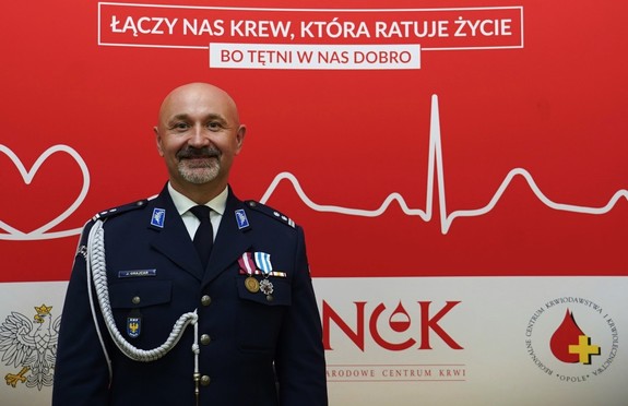 wyróżniony medalem policjant na tle baneru z logo Honorowego Krwiodowstwa