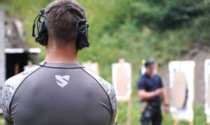 Policjant, a w tle instruktor przy tarczy strzeleckiej.