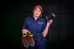 policjantka z butami do wędrówek górskich w jednej dłoni, w drugiej trzymająca aparat fotograficzny, w studio radiowym