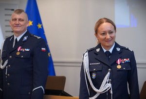 Zdjęcie: dwóch policjantów, za nimi flaga niebieska.