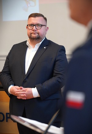 Zdjęcie: mężczyzna stojący w garniturze.