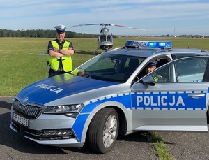 Zdjęcie: radiowóz na pierwszym planie, za nim helikopter.