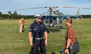Zdjęcie: policjant wypowiada się do mikrofonów, za nim śmigłowiec.