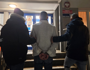 Dwaj mężczyźni prowadzą mężczyznę w kajdankach