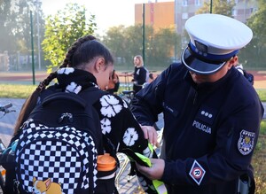 zdjęcie kolorowe: policjanci rozdają dzieciom kaski i elementy odblaskowe