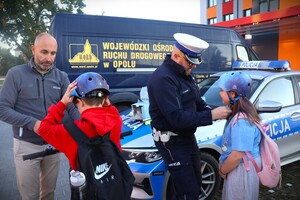 zdjęcie kolorowe: policjanci rozdają dzieciom kaski i elementy odblaskowe