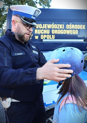 zdjęcie kolorowe: policjanci rozdają dzieciom kaski i elementy odblaskowe