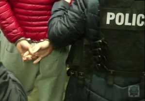 Policjantka i zatrzymany, który na ręce trzymane z tyłu ma założone kajdanki