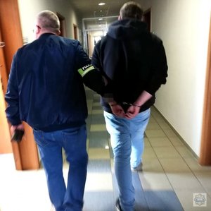 Policjant słuzby kryminalnej prowadzi zatrzymanego 22-latka korytarzem komendy policji