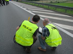 dwóch policjantów kuca na drodze - prowadzą pomiary na miejscu wypadku drogowego