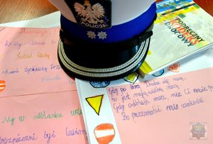 czapka policjanta ruchu drogowego a obok prace konkursowe; rymowanki napisane odręcznie na kartkach papieru