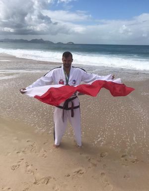 Mateusz Rojowski stoi w stroju sportowym na plaży i trzyma flagę Polski