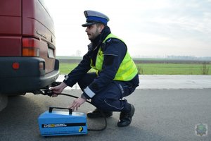 policjant kuca przy samochodzie i urządzeniem mierzy emisję spalin