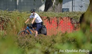 policjant jedzie na rowerze obok krzaki