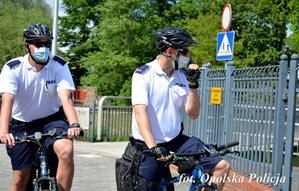 dwóch policjantów na rowerze, jeden trzyma w ręku radiostację