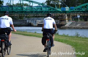 jedzie obok siebie w parku dwóch policjantów na rowerze