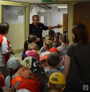 dzieci w korytarzu w tle policjant zaprasza je do wejścia