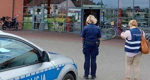 stoją obok siebie policjantka z pracownicą sanepidu przed budynkiem supermarketu
