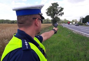 policjant stoi przy drodze i trzyma miernik prędkości
