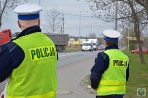 2 policjantów ubranych w kamizelki odblaskowe stoi przy drodze