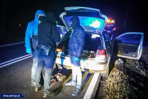 zamaskowani policjanci stoją przy otwartym bagażniku samochodu