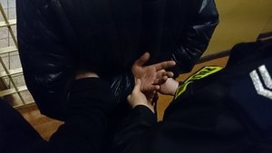 mężczyzna z kajdankami na rękach obok stoi policjant