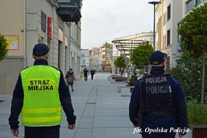 policjant ze strażnikiem miejskim sprawdzają przestrzeganie obostrzeń