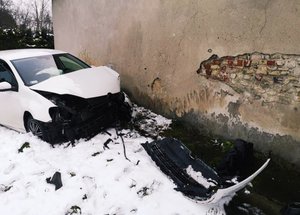 biały samochód osobowy z rozbitym przodem stoi przy ścianie budynku