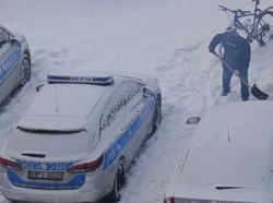 radiowóz na zaśnieżonym parkingu obok człowiek z łopata do odśnieżania