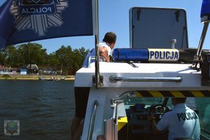 łódka na niej flaga z gwiazdą policja w tle policjant na łodzi odwrócony tyłem i drugi policjant w kabinie za starami