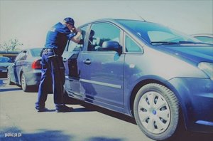 umundurowany policjant zagląda do wnętrza zaparkowanego samochodu